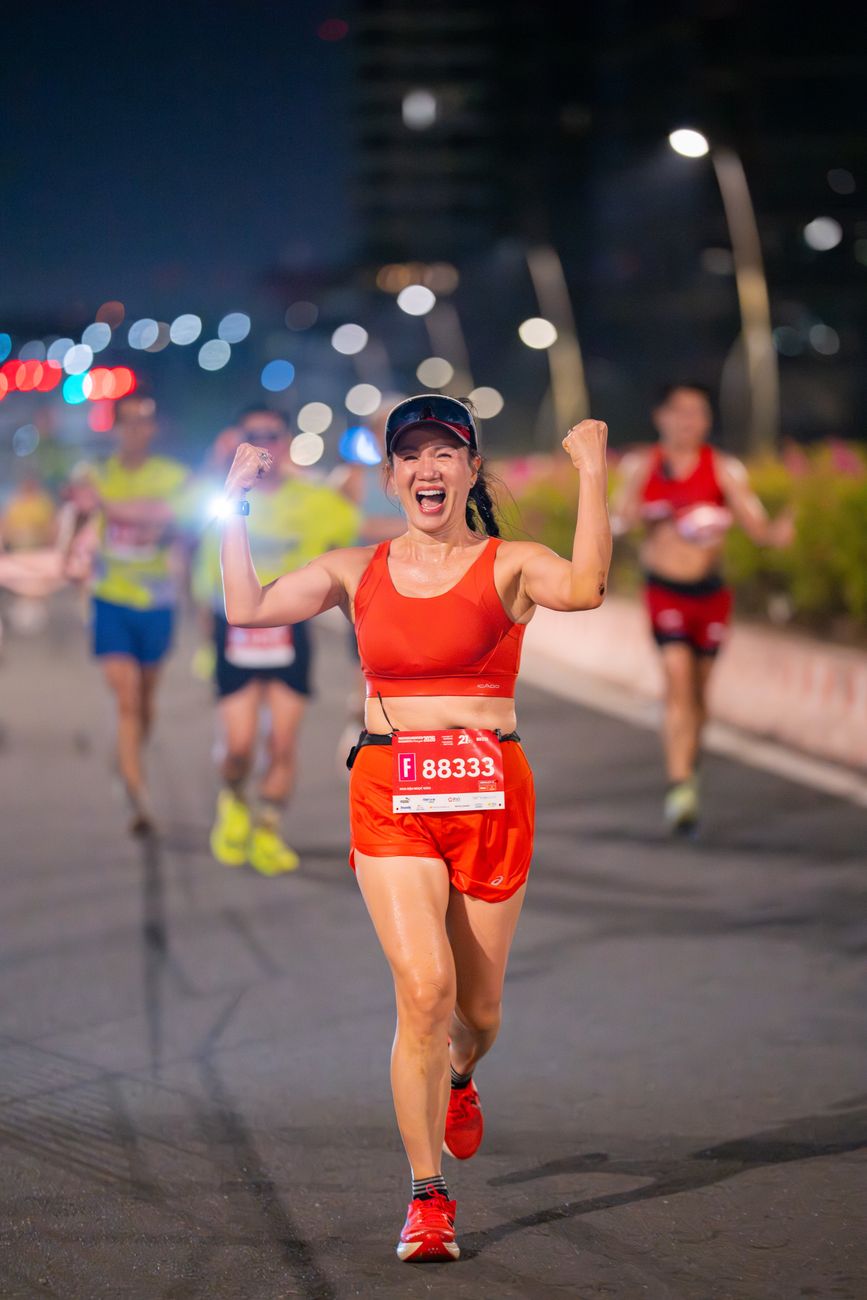 A runner celebrating with both fists raised on a floodlit finish straight